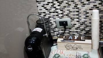 Un coin cuisine équipé d’une machine à café, d’une boîte étiquetée « CAFÉ » et d’un dosseret carrelé.