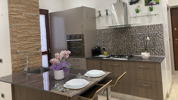 A modern kitchen with a glass dining table, built-in appliances, and decorative plants. - Orchid Apartment (Castiglione Olona)
