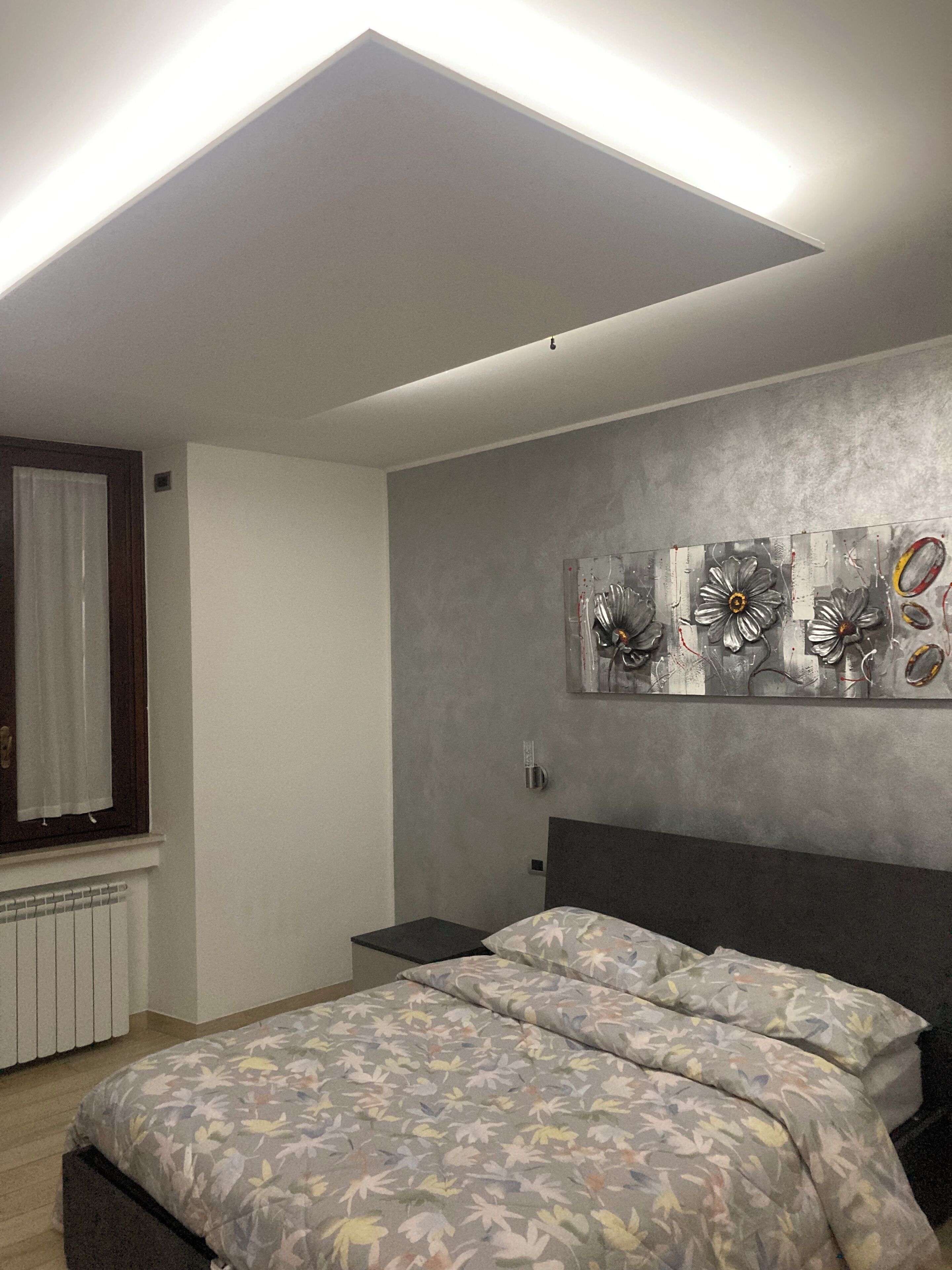A bedroom with a bed, a nightstand, a wall-mounted artwork, and a window with curtains.