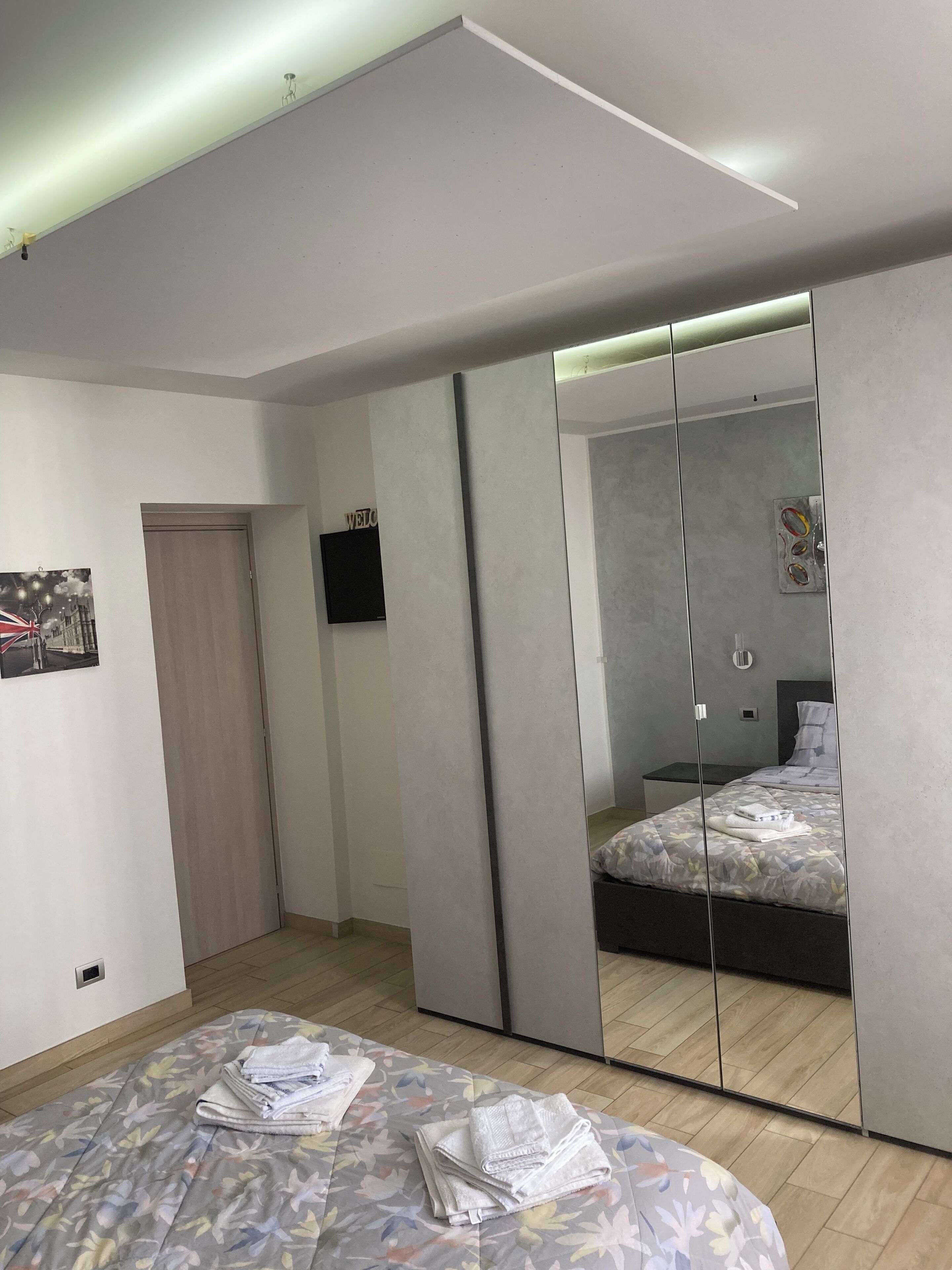 Une chambre à coucher moderne avec un grand miroir, un lit recouvert d’une couvre-lit à motifs floraux et une petite table de chevet.