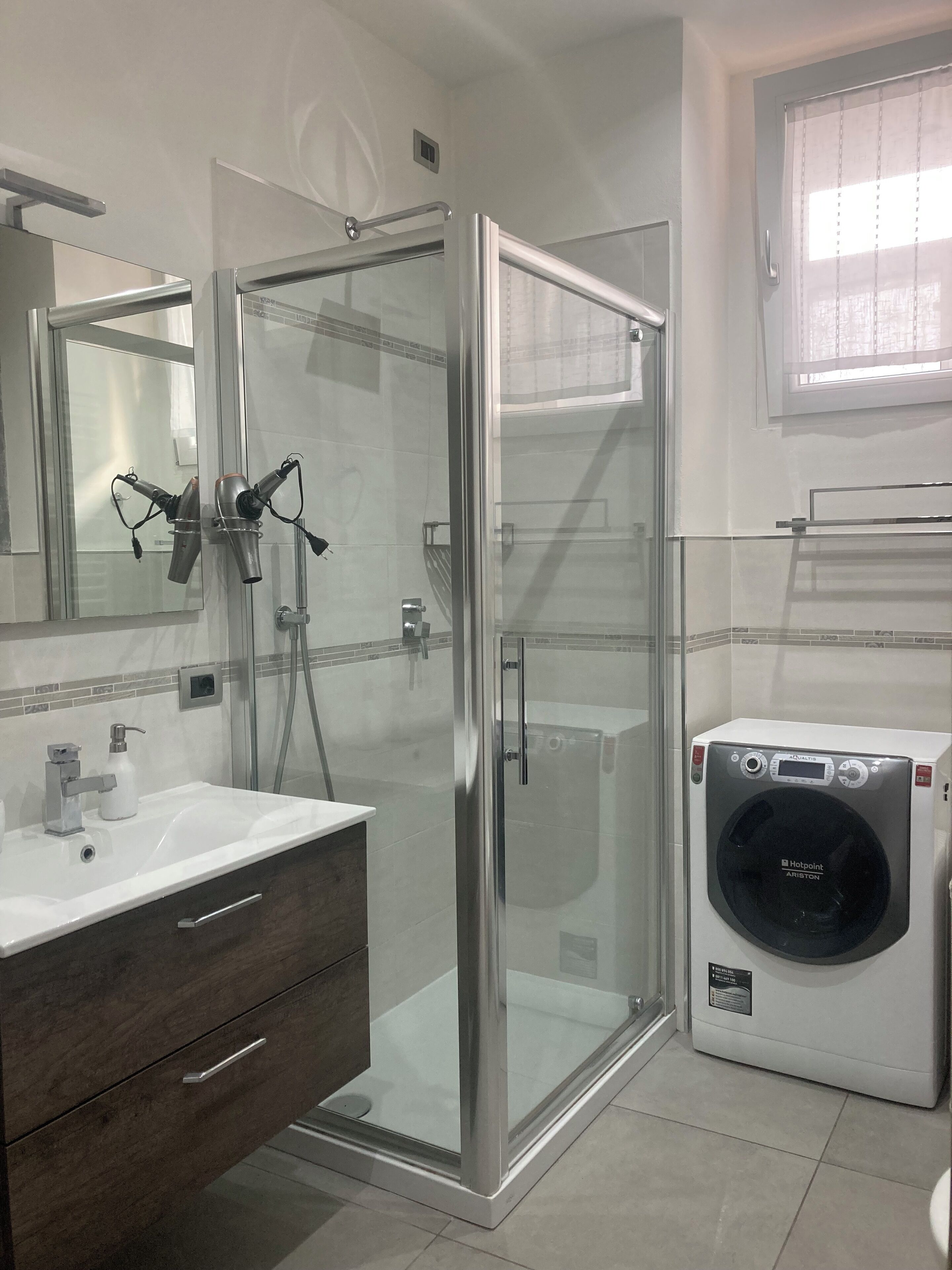 A modern bathroom with a glass-enclosed shower, a white sink with a mirror, and a built-in washing machine.