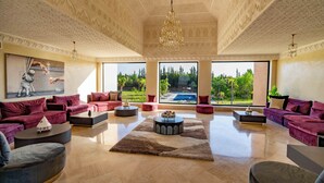 A spacious living room with a large window, a chandelier, and multiple sofas. - Palais Nouhass (Marrakech)