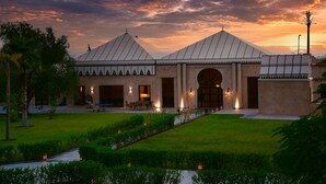 A building with a large arched entrance, a covered patio area, and a well-maintained lawn with decorative lighting. - Palais Nouhass (Marrakech)