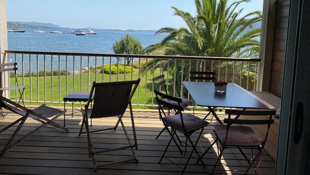 A balcony with a table and chairs, overlooking a body of water with boats and palm trees. - Waterfront apartment, Porto-Vecchio (Porto-Vecchio)