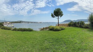 A grassy area with a single tree, a body of water, and distant mountains. - Waterfront apartment, Porto-Vecchio (Porto-Vecchio)
