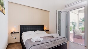 Un dormitorio moderno con una cama grande, una mesita de noche con lámpara y una puerta corrediza de vidrio que da a un área de estar exterior.