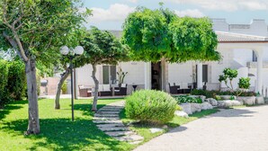 Un edificio con un camino empedrado que conduce a una entrada cubierta, rodeado de vegetación y macetas de piedra.