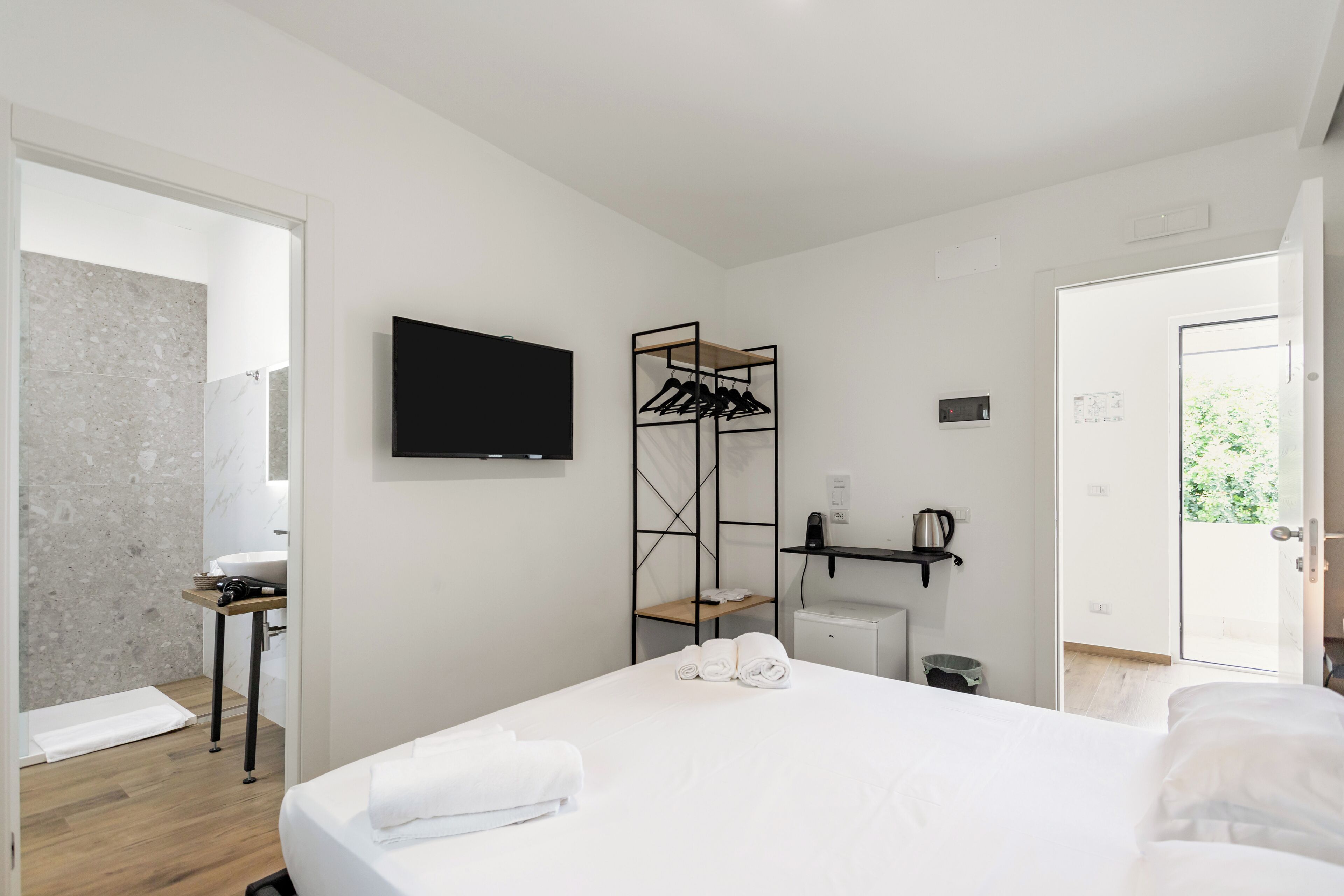 A modern hotel room with a bed, a TV, a wall-mounted towel rack, and a small table with a kettle.