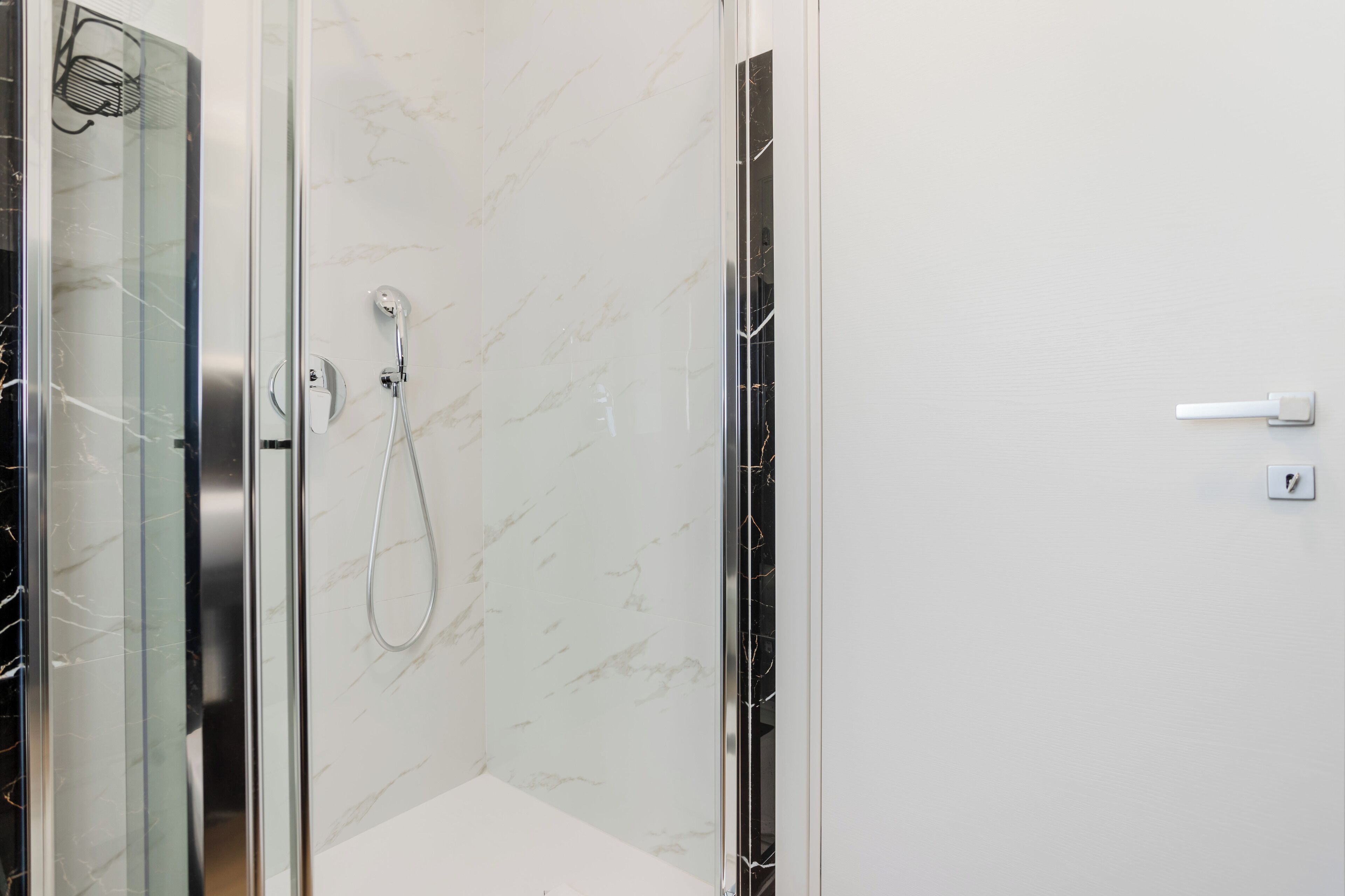 A modern bathroom with a glass shower enclosure, a marble wall, and a white door.