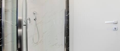 A modern bathroom with a glass shower enclosure, a marble wall, and a white door.