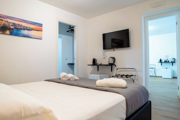 A modern hotel room with a bed, a flat-screen TV, a coffee machine, and a desk with a chair. - Pietramare Luxury suites (Bari)