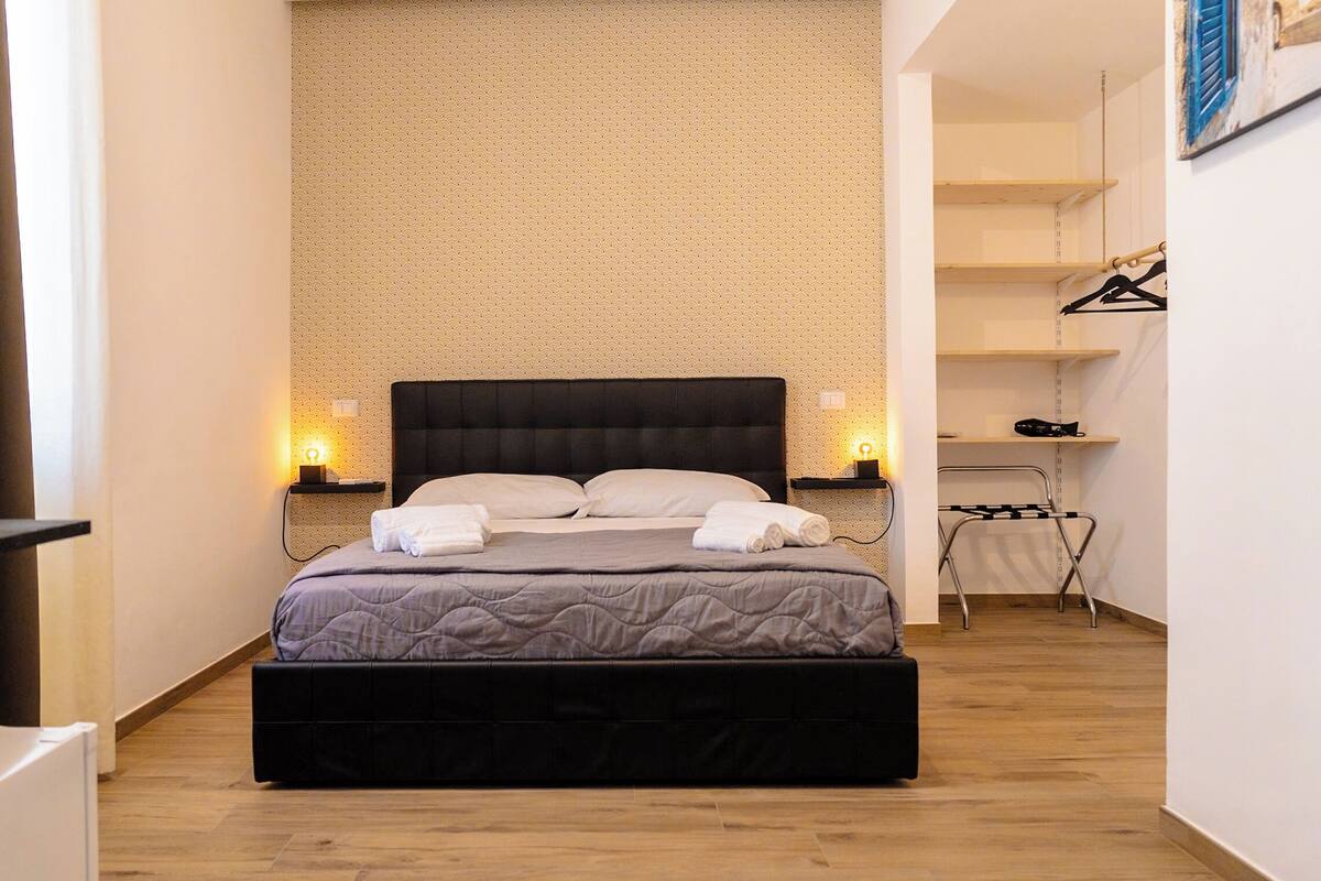 A neatly arranged bedroom with a large bed, bedside lamps, a hanging shoe rack, and a radiator.
