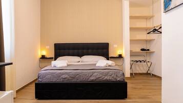 Un dormitorio ordenado con una cama grande, lámparas de noche, un perchero para zapatos y un radiador.