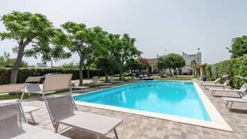 A rectangular swimming pool with a tiled deck, surrounded by lounge chairs and trees.