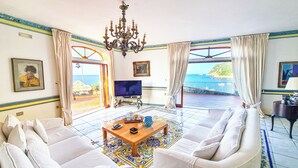Een zithoek met een bank, een televisie, een kroonluchter en uitzicht op zee.
