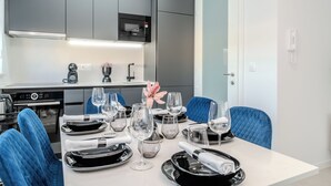 A modern kitchen with grey cabinets, a microwave, and a coffee machine. There is a dining table set with plates, glasses, and a decorative flower. Blue upholstered chairs are around the table. - Two-bedroom apartment with a terrace (Novalja)