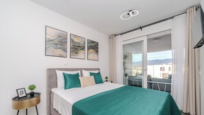 A modern bedroom with a large bed, a small side table with a plant, and a balcony with a view. - Two-bedroom apartment with a terrace (Novalja)