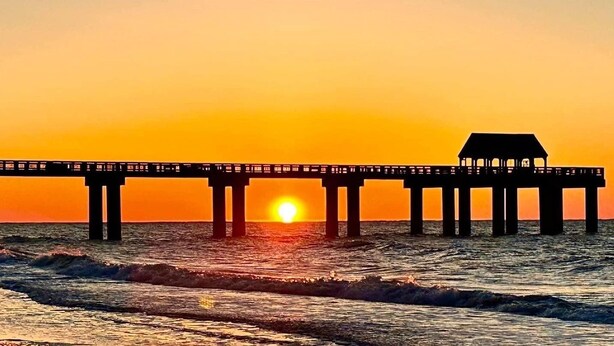 Un muelle que se adentra en el agua, con un atardecer al fondo.