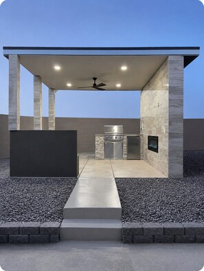 An outdoor kitchen area with a grill, oven, and built-in fire feature, under a covered structure with a ceiling fan. - Charming and Cozy Place (Las Vegas)