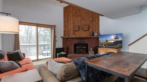 Un salon chaleureux avec une cheminée, un ensemble de canapés et un téléviseur diffusant un paysage pittoresque.