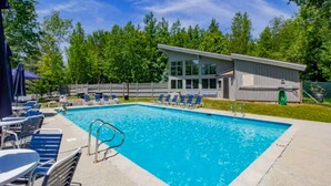 Une piscine rectangulaire à l’eau bleue, entourée de chaises longues et d’un petit bâtiment doté de grandes fenêtres.