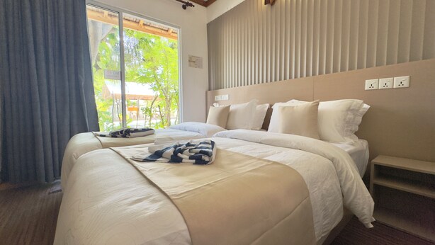 A hotel room with a large bed, a window with a view of greenery, and a wall with a power outlet. - Navaya Dhiffushi (Dhiffushi)