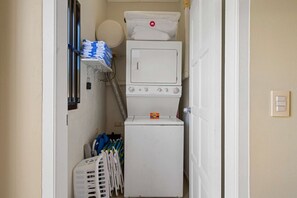 A laundry area with a washing machine, a dryer, and a stack of folded towels. - Luxurious 2-Bedroom Condo near Eagle Beach - Noord (Noord)