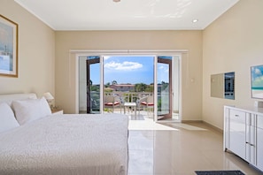 Ein Hotelzimmer mit Bett, Fernseher, Balkon mit Blick auf die Stadt und einer Essecke mit Stühlen und Tisch.