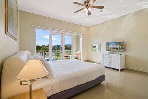 A bedroom with a bed, a ceiling fan, a TV, and a balcony with a view of the outside. - 2BR Townhouse w/ Pool View, 1 Min to Eagle Beach (Noord)