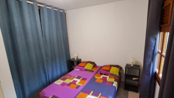 Un dormitorio con una cama, dos mesitas de noche y una ventana con cortinas.