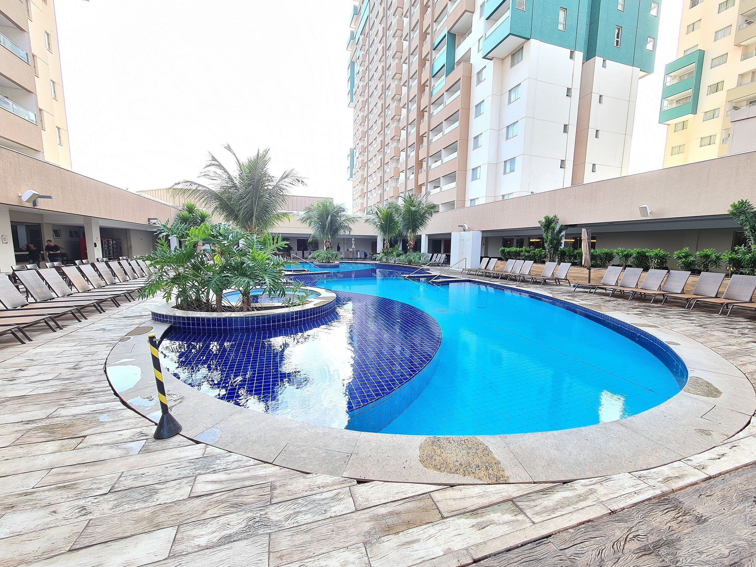 A swimming pool with lounge chairs and palm trees, surrounded by multi-story buildings.