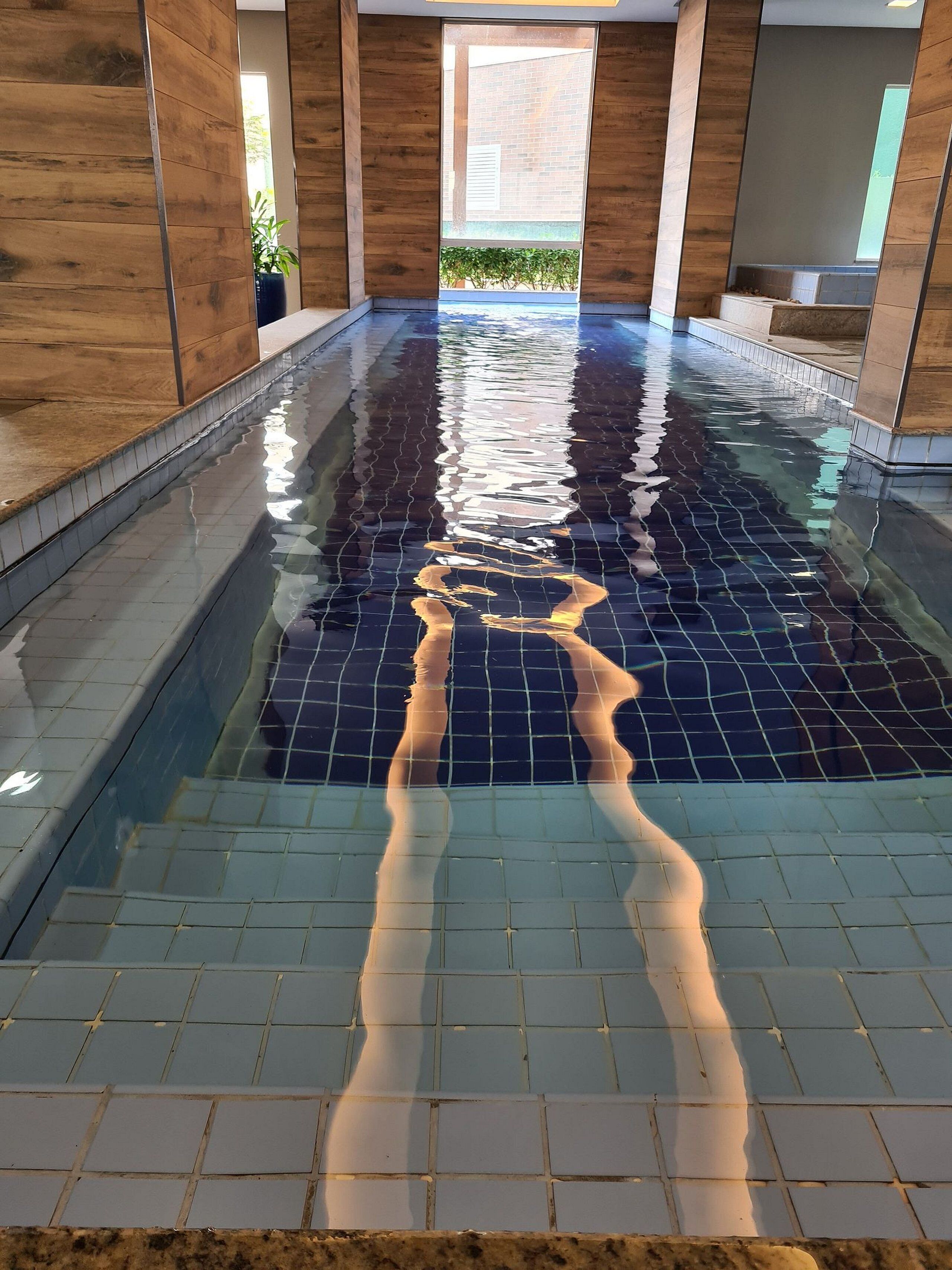Piscina com piso azulejado e superfície de água cristalina.