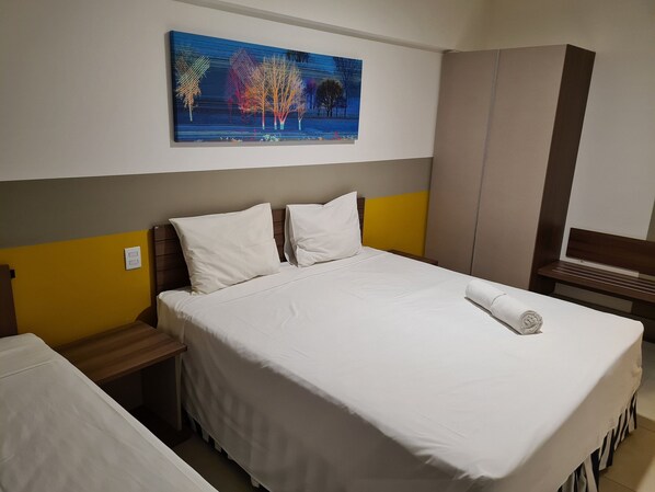 Een hotelkamer met een bed, nachtkastje, kledingkast en een schilderij aan de muur.
