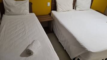 Quarto de hotel com duas camas de solteiro, cada uma com roupa de cama e almofadas brancas, uma mesa de cabeceira de madeira e uma parede amarela como detalhe.