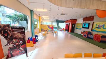 A spacious indoor play area with colorful play structures, seating areas, and a large mural on the wall.