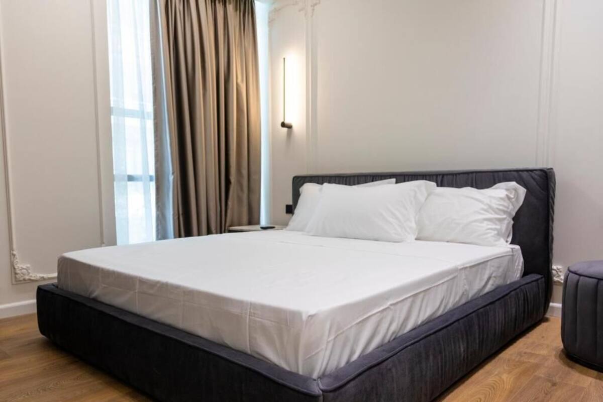 A modern bedroom with a large bed, a bedside table, and a window with curtains.
