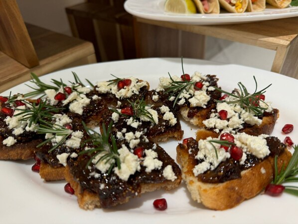 A plate of bruschetta topped with a dark spread, crumbled cheese, and garnished with rosemary and pomegranate seeds. - Adore Boutique Hotel (Vlorë)