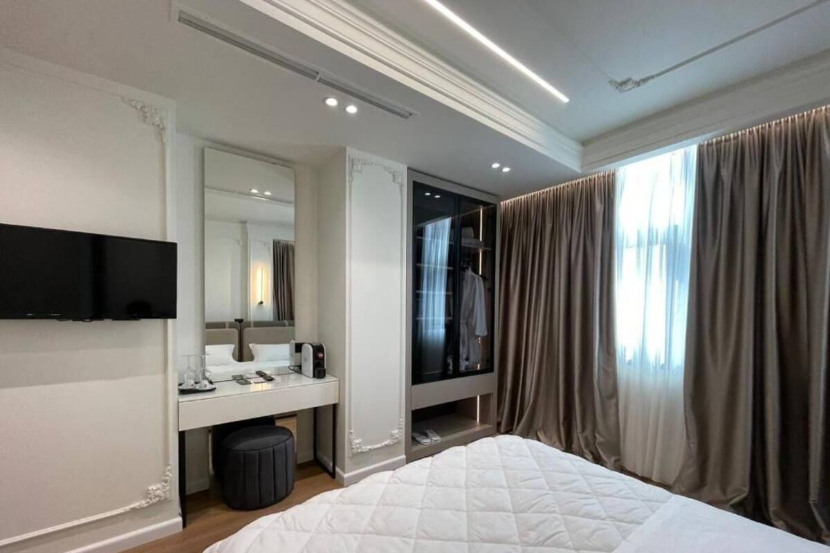 A modern hotel room with a large bed, a vanity with a mirror, a television, and a walk-in closet.
