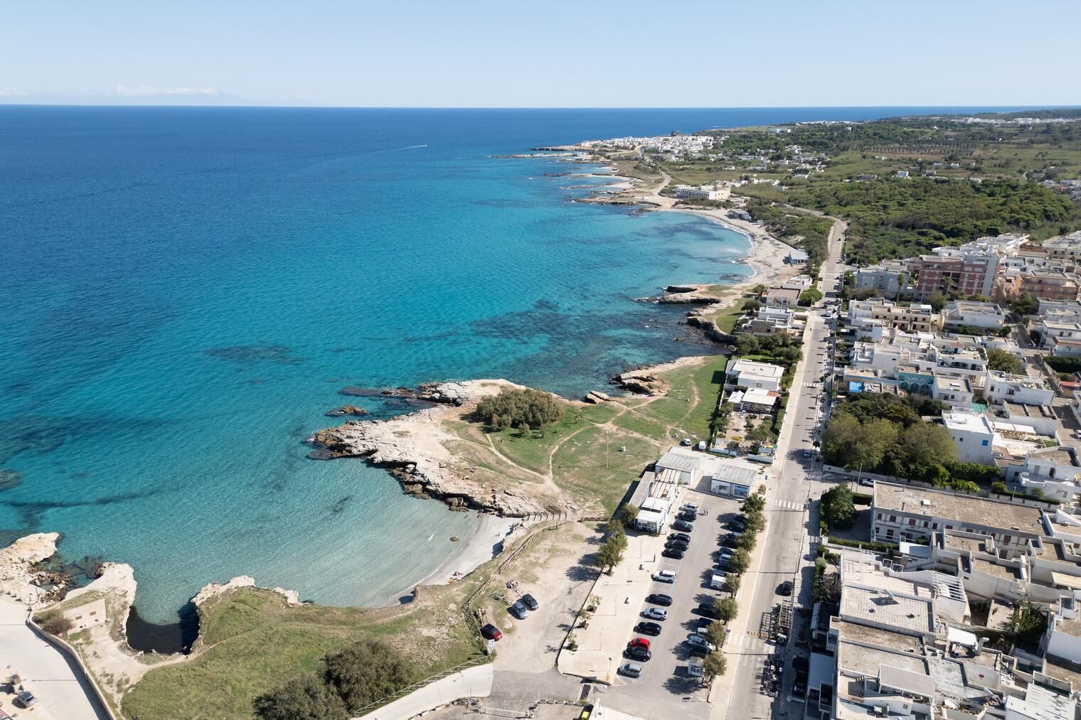 Vista aérea de un pueblo costero con mar azul cristalino, costa rocosa y una combinación de edificios residenciales a lo largo de la orilla.