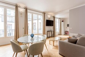 Uma sala de estar moderna com uma mesa de jantar redonda, dois sofás e uma televisão fixada na parede.