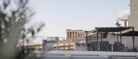 A rooftop terrace with a metal fence, a view of the cityscape, and a building with a modern design.