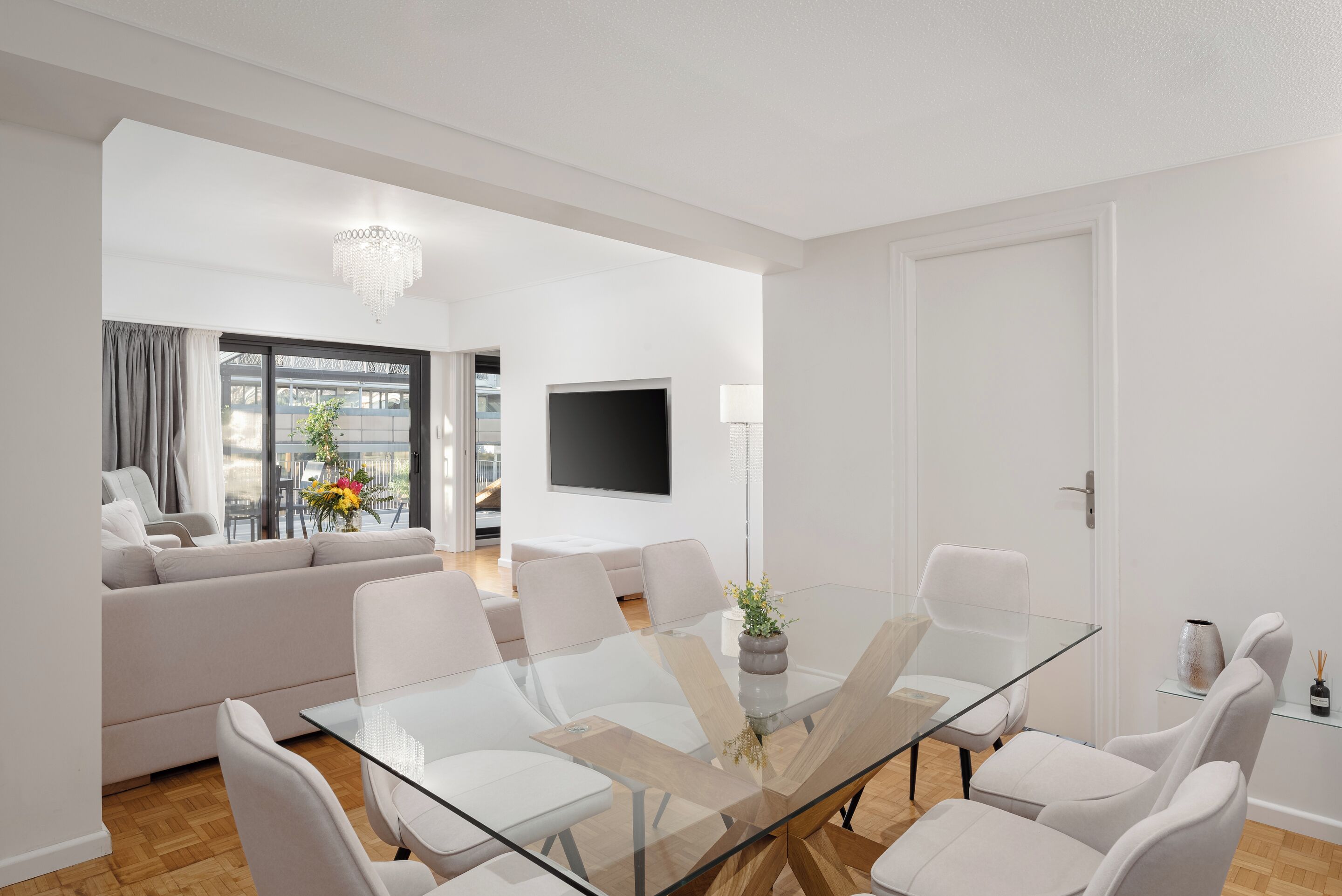 Un salon moderne avec une table à manger en verre, des canapés blancs et un téléviseur à écran plat.