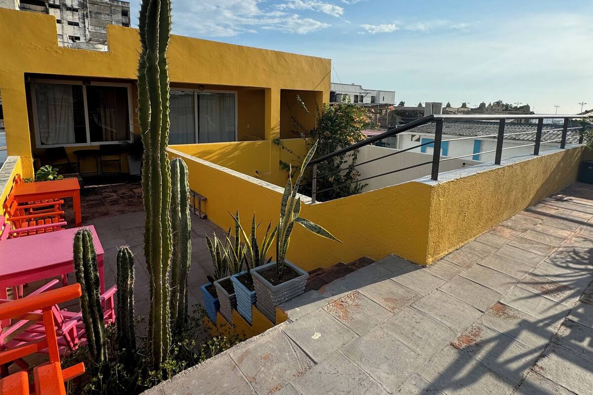 A yellow building with a flat roof, outdoor seating, and cacti.