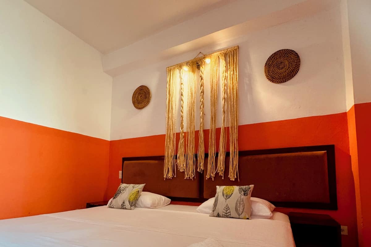 A hotel room with a large bed, two bedside tables, and a headboard with a decorative hanging.