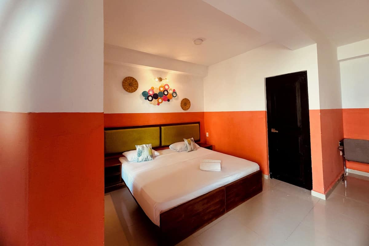 A hotel room with a large bed, a headboard, a wall-mounted light fixture, and a door.