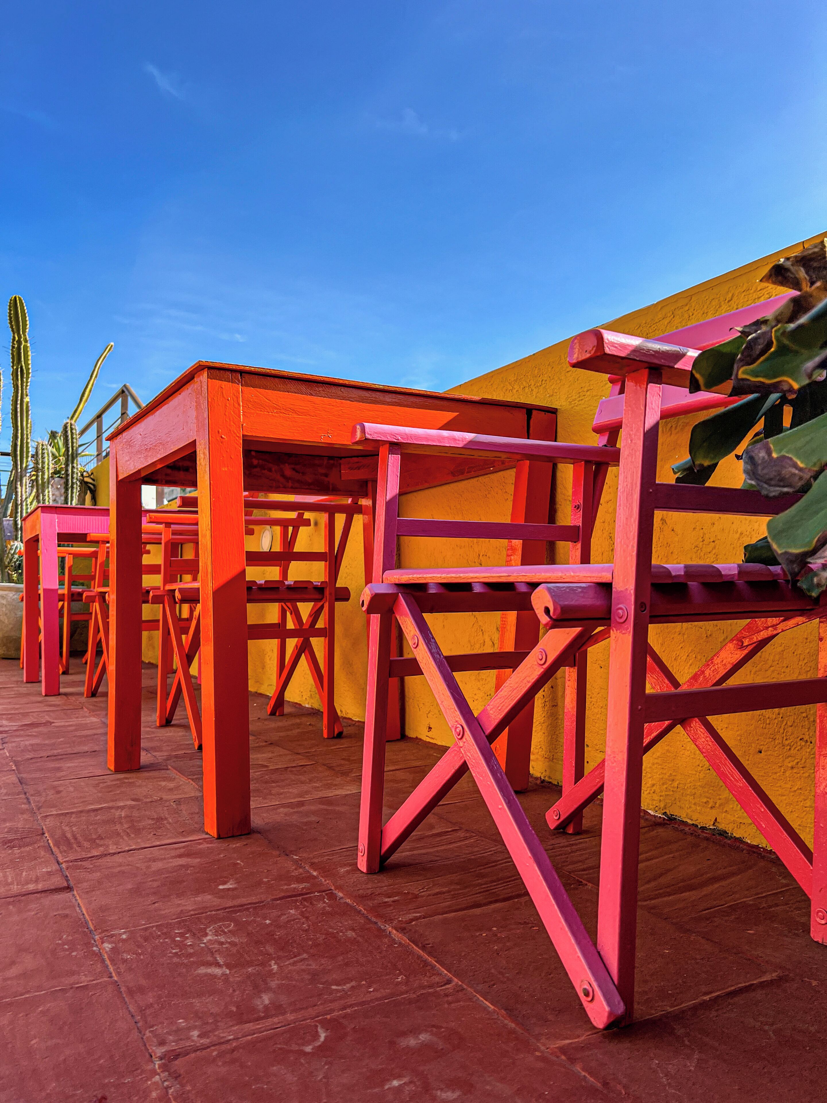 Outdoor wooden furniture with a vibrant yellow wall in the background.