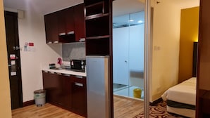 Ein kleines Hotelzimmer mit Küchenzeile, einem Bett und einem durch eine Glastür einsehbaren Badezimmer.