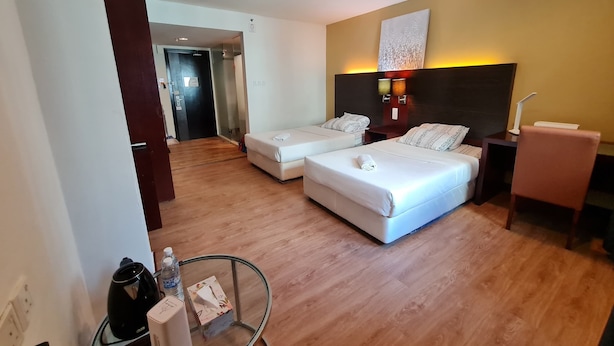 Ein Hotelzimmer mit zwei Betten, einem Nachttisch, einem Sessel, einem Schreibtisch und einer Wandlampe.