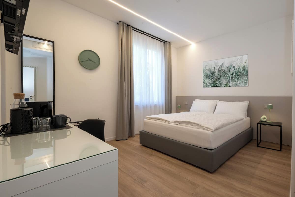 Quarto de hotel moderno com uma cama, mesa de cabeceira e escrivaninha com máquina de café.