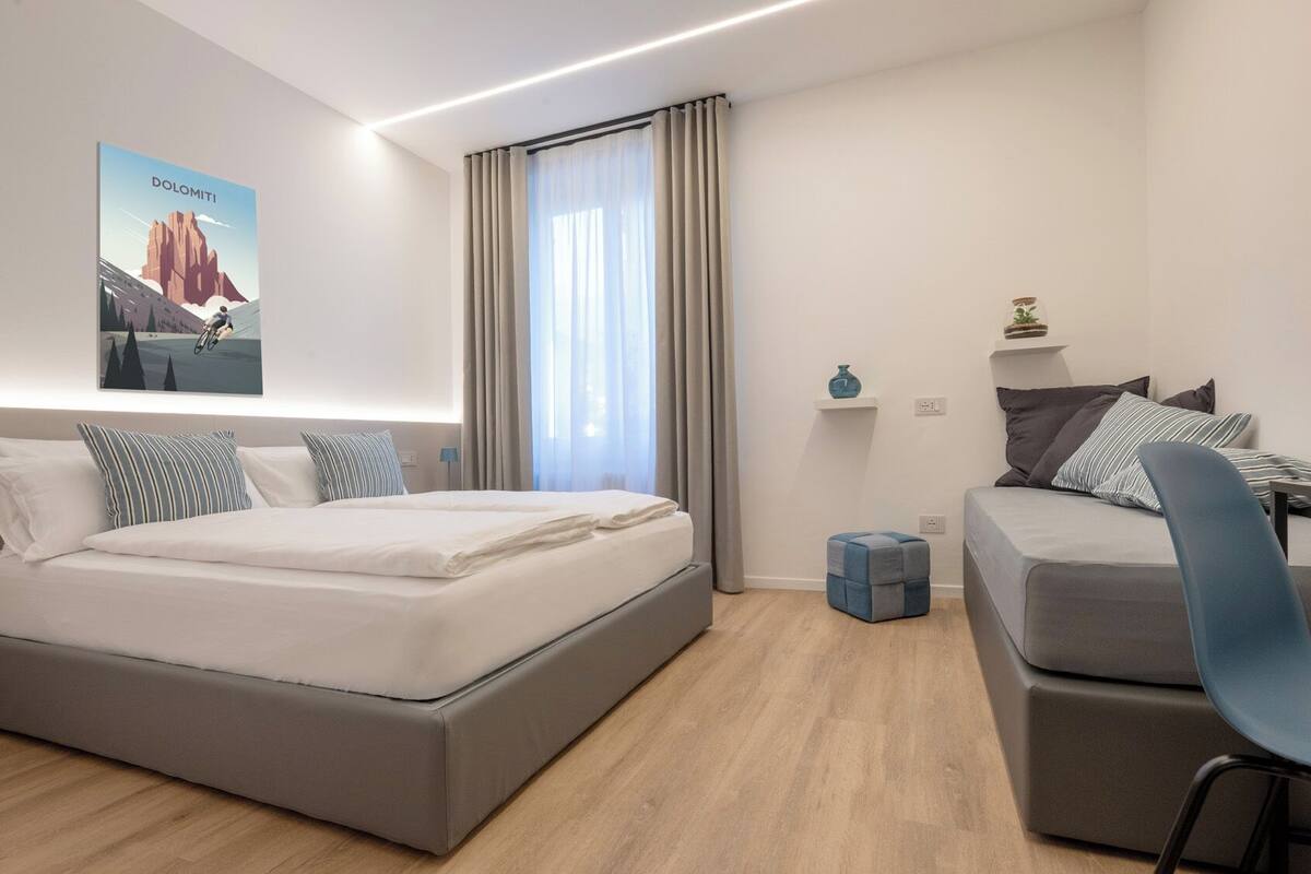 Quarto de hotel moderno com uma cama grande, um sofá menor, uma escrivaninha e uma janela com cortinas.